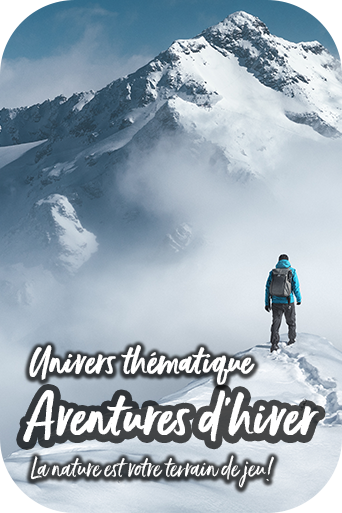 Une personne en tenue d’hiver se tient dans un paysage de montagne imposant, rempli de neige et de brouillards, et contemple un massif montagneux.