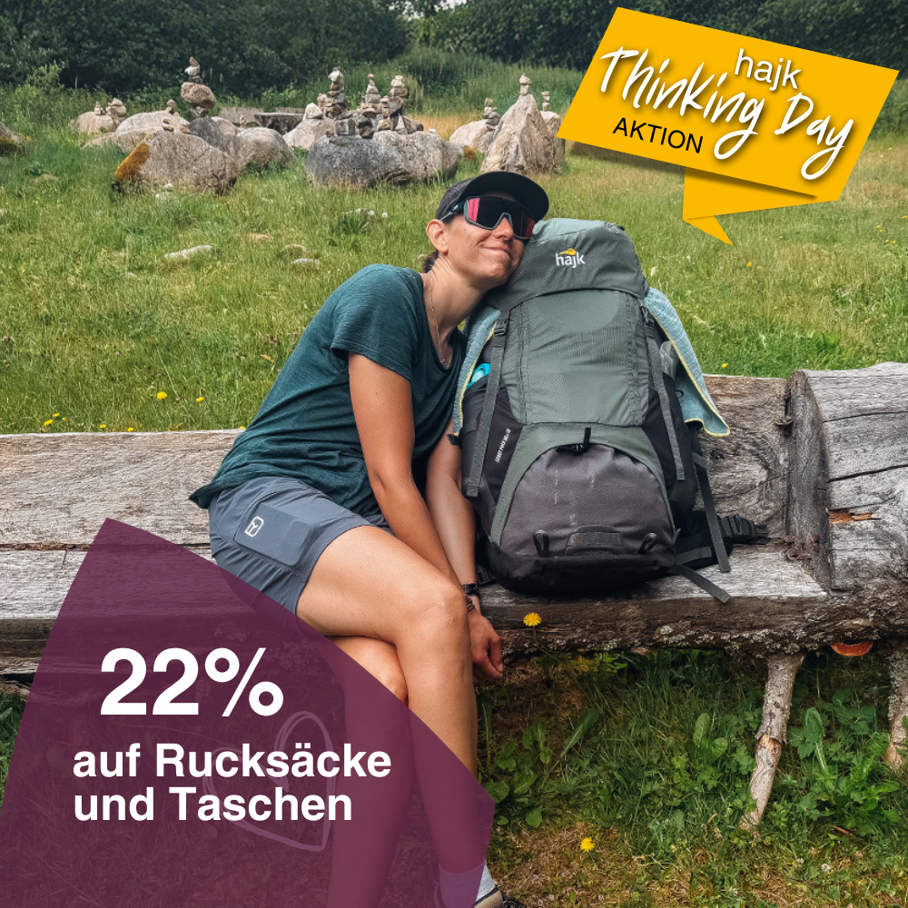 Eine junge Frau im Wanderoutfit kuschelt sich auf einer Holzbank an ihren Trekkingrucksack.