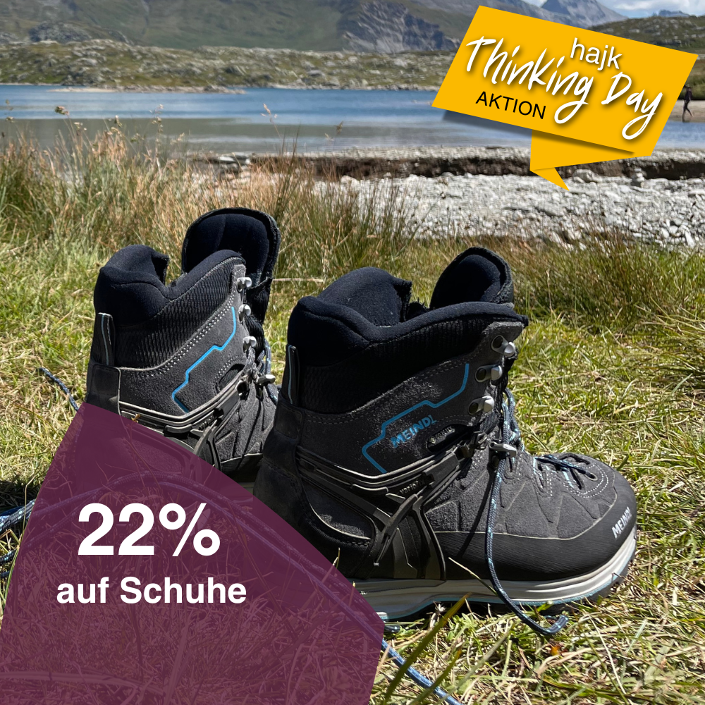 Nahaufnahme eines Paares Wanderschuhe, die auf einer Wiese an einem Bergsee stehen.