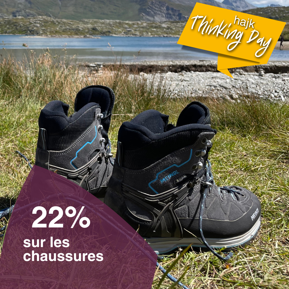 Vue rapprochée d'une paire de chaussures de randonnée posée sur une prairie au bord d'un lac de montagne.