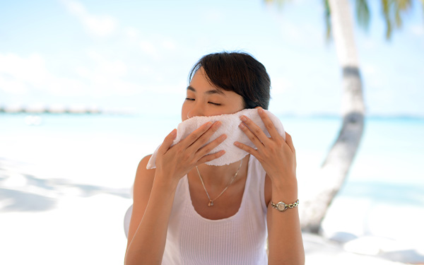 Frau hält sich an einem Strand ein weisses Handtuch ans Gesicht, um sich abzukühlen.