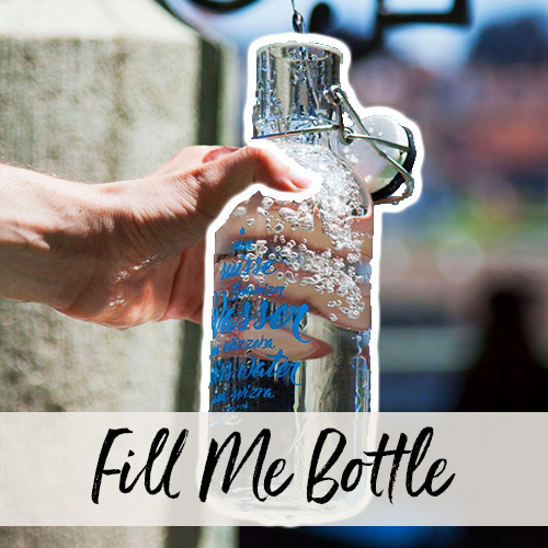 Gros plan d’une main tenant une bouteille Fill Me sous le jet d’eau d’une fontaine.