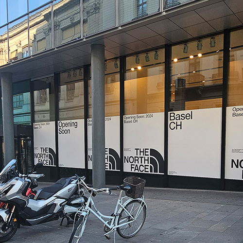 Vue extérieure de l'entrée principale du magasin The North Face à Bâle. Un scooter et un vélo sont garés devant.