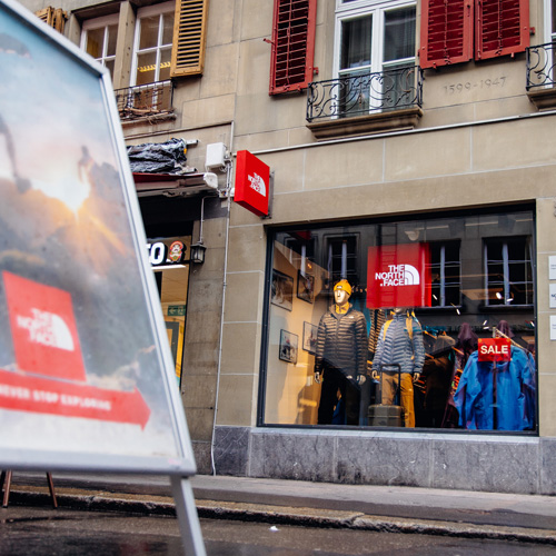 Vue extérieure de la vitrine du magasin The North Face à Berne. Un panneau publicitaire se trouve au premier plan.