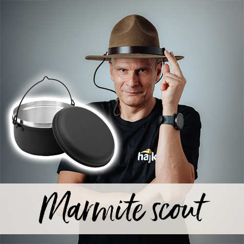 Homme portant un chapeau scout qui touche sa visière du doigt. Devant lui se trouve un chaudron scout avec son couvercle.