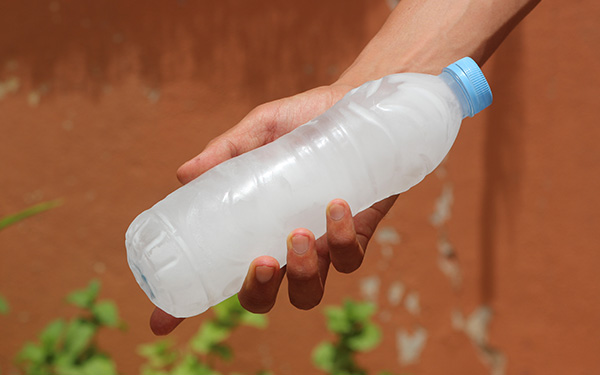 Nahaufnahme einer Hand, die eine PET-Flasche hält, deren flüssiger Inhalt zu Eis gefroren ist.