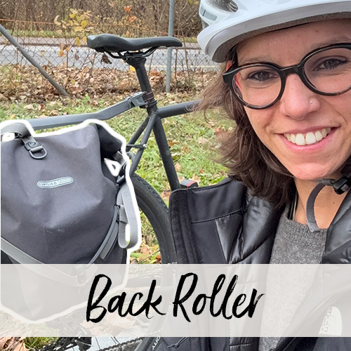 Une jeune femme portant un casque de vélo et des lunettes sourit à la caméra devant un vélo équipé d’une sacoche latérale.